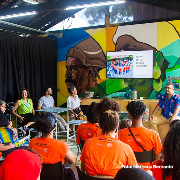 Roda de conversa em espaço com mural, participantes de camiseta laranja