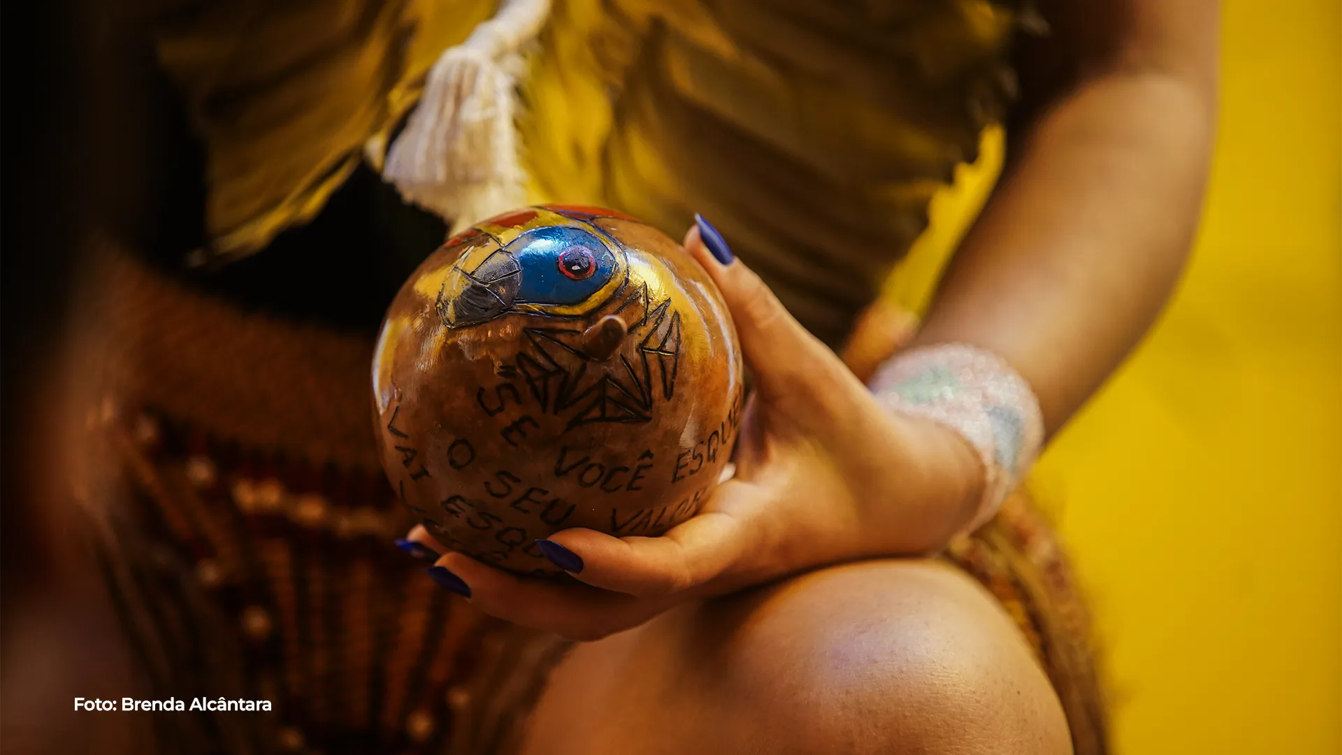 Mãos seguram um tambor pintado com motivos da mata